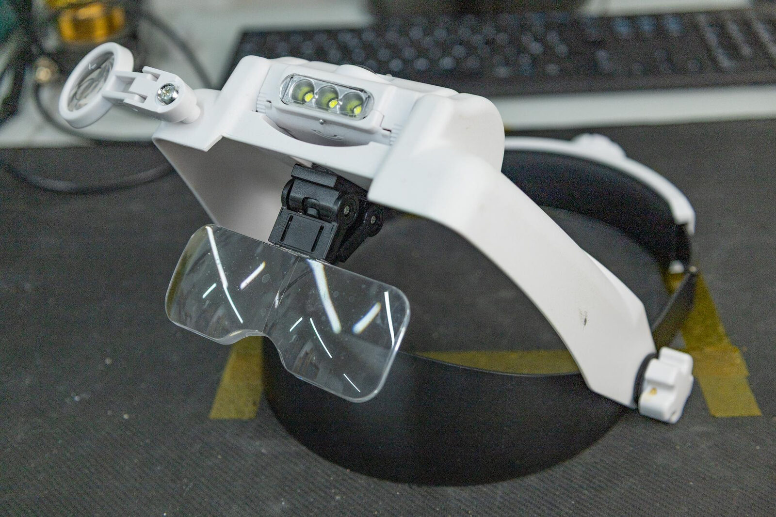 An LED head magnifier visor with interchangeable lenses and a swing-away loupe, resting on a workbench