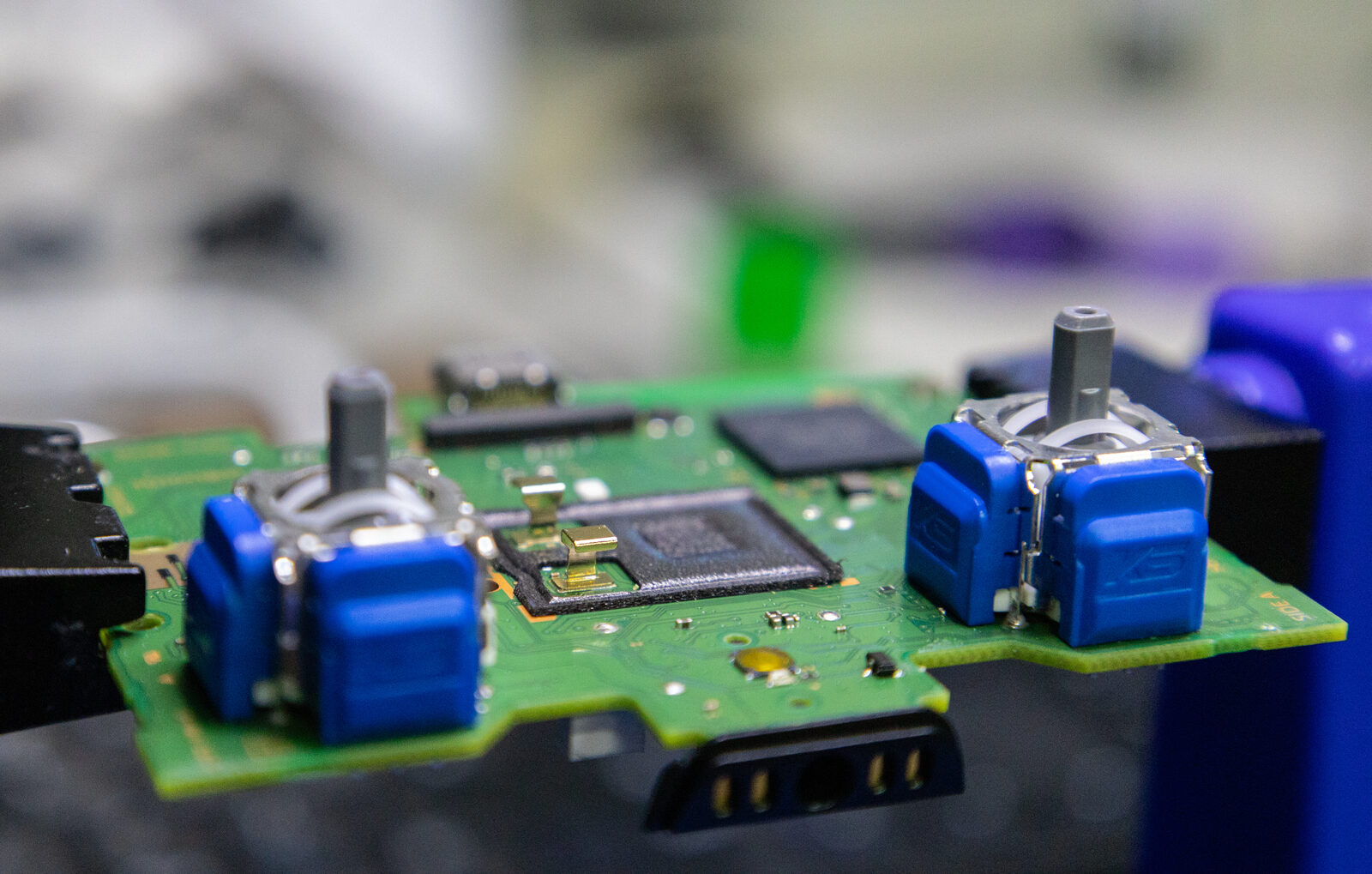 A DualSense circuit board with new blue joystick modules soldered in place