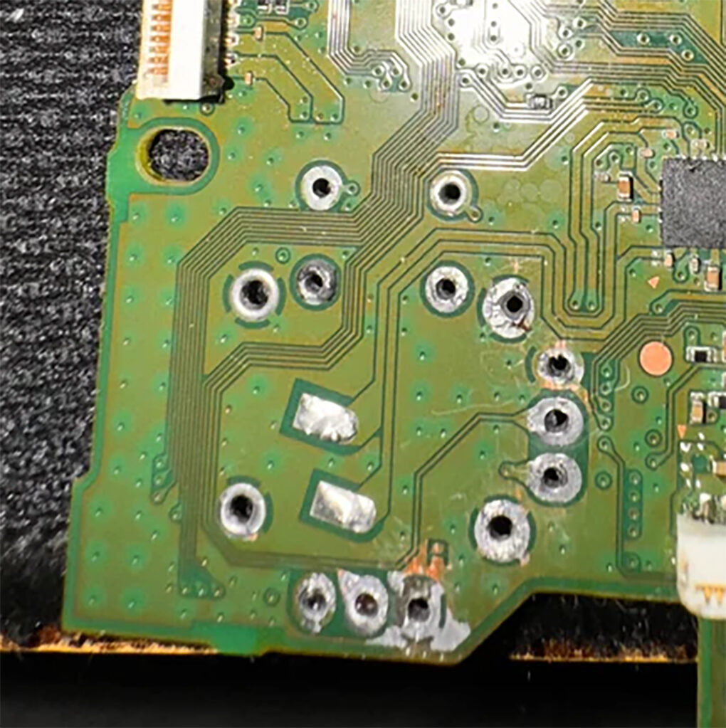 A PS5 DualSense board after joystick module removal, showing torn pads and solder mask scraped back to bare copper around the through-holes
